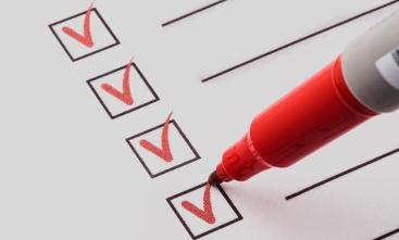 Quatro pequenos quadrados com uma linha ao lado, preenchidos com a letra v por uma caneta marca-texto vermelha, como um check box