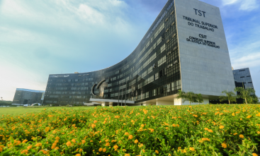 Fachada TST com jardim de pequenas flores na frente do prédio.  