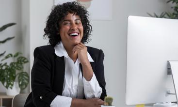 fotografia ilustrativa de uma mulher negra sorrindo de frente a um computador