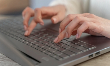 Fotografia ilustrativa de mãos femininas digitando no teclado de um notebook