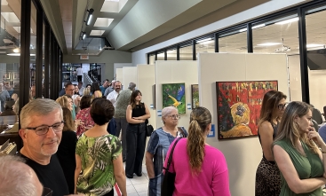 Exposição de arte com quadros coloridos de animais e paisagens, em ambiente moderno, onde um público diverso aprecia as obras.