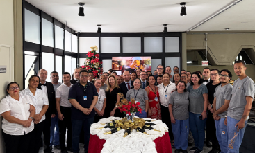 Dezenas de pessoas reunidas em torno de uma mesa com decoração natalina, a maioria delas vestindo uniforme branco ou cinza