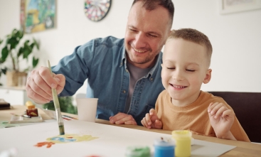 Pai e filho pintando uma folha com pincéis e tintas