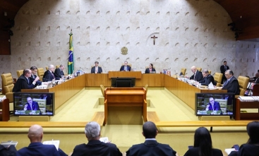 Plenário do Supremo Tribunal Federal. 11 ministros dispostos em uma grande mesa em formato de U. Ao fundo, a bandeira do Brasil, o brasão da Justiça e um crucifixo