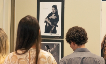 Duas pessoas, um homem e uma mulher, de costas, olhando para uma exposição fotográfica na qual as fotos são retratos em preto e branco de mulheres.