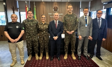 Sete pessoas em frente a uma escrivaninha posando para fotos. Três vestem terno e gravata e outros três uniformes do exército.
