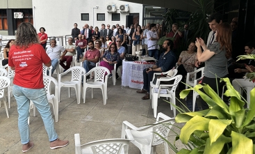 Pessoa de camiseta vermelha falando para um público sentado em cadeiras