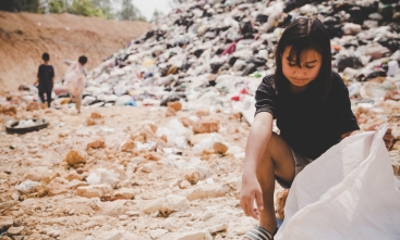 Menina aparentando ser do continente asiático, de cerca de 10 anos, cata resíduos em um lixão 