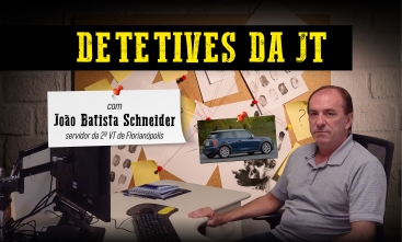 Detetives da JT: João Batista Schneider, servidor da 2ª VT de Florianópolis. Um homem branco sentando à mesa de trabalho, vestindo camisa polo cinza e olhando para a câmera