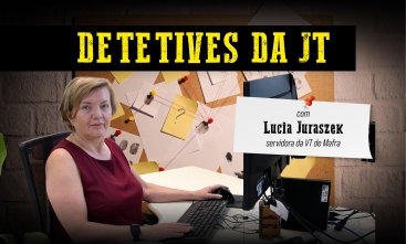 Detetives da JT: Lúcia Juraszek, servidora da VT de Mafra. Uma mulher de blusa vinho, loira, cabelos curtos, com um leve sorriso, em frente a um monitor. Ao fundo, um quadro com diversos papeis pendurados, como se estivesse em uma delegacia