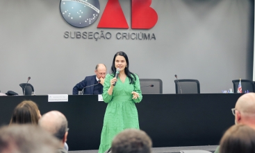 Uma mulher de vestido verde fala ao microfone para uma plateia 