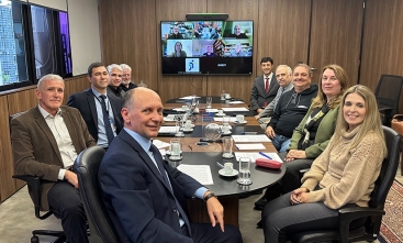 Oito homens e duas mulheres estão sentadas em uma mesa oval de reunião, sorrindo para a foto