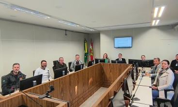 Grupo de homens e duas mulheres posam para foto, sentados ao redor de uma mesa em uma sala de audiências