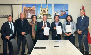 Duas mulheres e cinco homens estão em pé, sorrindo e posando para a foto, em uma sala de reuniões com quadros coloridos na parede