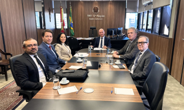 Cinco homens e uma mulher estão sentados em uma mesa de reunião oval, posando para a foto