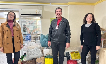 Três pessoas em pé posando par foto diante de bolsas com cobertores e roupas de inverno
