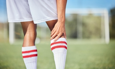 Fotografia ilustrativa com close de um jogador de futebol segurando o joelho direito