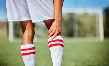 Fotografia ilustrativa com close de um jogador de futebol segurando o joelho direito