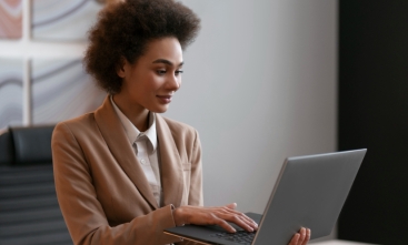 Fotografia ilustrativa de mulher negra vestida formalmente utilizando o notebook em um escritório