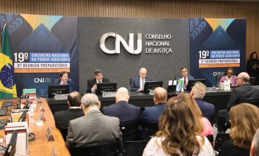 Quatro homens e uma mulher estão sentados em uma mesa de uma palestra. Pessoas estão assistindo. No fundo do palco tem um painel com o texto: CNJ