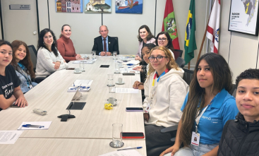 Seis jovens e cinco adultos estão sentados em uma mesa de reunião oval, posando para a foto