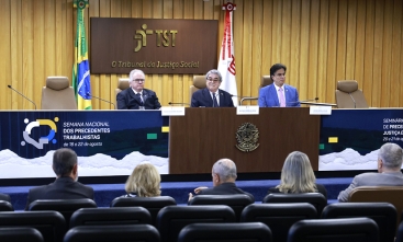 Três homens de terno sentados em uma mesa em um evento.