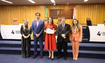 Fotografia na qual cinco pessoas posam em auditório do TST; ao centro, mulher segura certificado