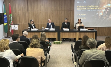 Mesa composta de quatro pessoas e público em primeiro plano assistindo palestra