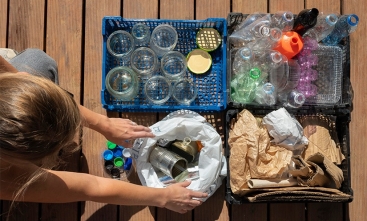 Fotografia ilustrativa em que pessoa separa resíduos recicláveis em caixas