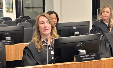 Foto de uma mulher loira, sentada em um tribunal, vestida com toga
