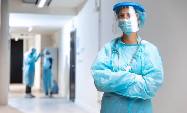 Foto de uma profissional de saúde vestida com equipamentos de proteção individual, em um ambiente hospitalar