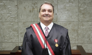 imagem de um senhor de meia idade, usando toga, faixa e medalha. Ele tem cabelo e bigode pretos