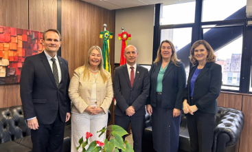 Dois homens de terno e gravata e três mulheres vestidas formalmente estão em pé, posando para a foto