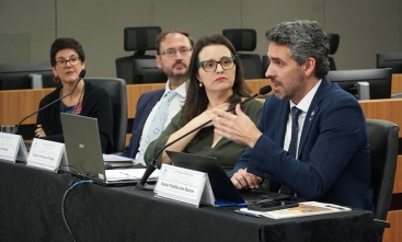 Palestrantes participam de mesa-redonda em auditório, com notebooks e microfones sobre a mesa.