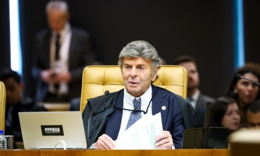 Foto do ministro do STF, Luiz Fux (homem de cabelo grisalho), sentado em uma mesa