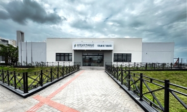 Prédio térreo em cor cimento queimado, ladeado por dois gramados. Céu nublado