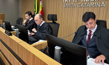 Fotografia de três homens sentados à bancada, analisando processos no plenário do TRT-SC