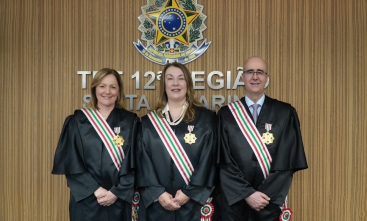 Três pessoas usando toga, uma faixa em torno dela e uma medalha fixada na toga