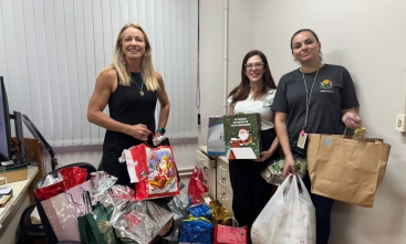 Foto de três mulheres exibindo presentes que foram entregues à entidade