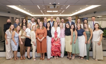 Grupo de 26 pessoas em pé, distribuídos em duas fileiras, posam para a foto em um auditório amplo