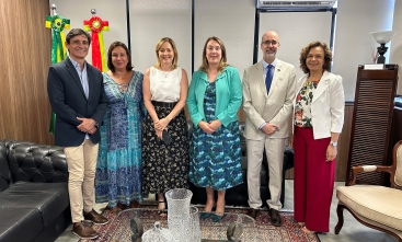 Quatro mulheres e dois homens, todos de pé, posam para a foto em uma pequena sala com bandeiras do Brasil e de SC ao fundo