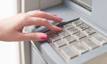 Foto que mostra a mão de uma mulher digitando no teclado de um caixa automático