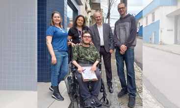 Cinco pessoas posam na calçada; jovem em cadeira de rodas segura prancheta.