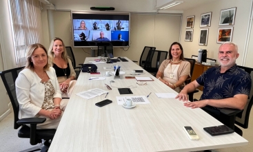 Grupo de pessoas sentadas ao redor de uma mesa branca posam para a foto