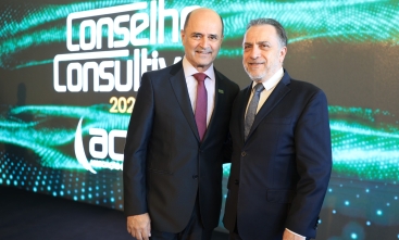 Dois homens de terno posam para a foto em frente a um telão digital