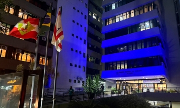 Foto mostra cinco pavimentos do prédio-sede do TRT-SC, iluminado de azul escuro, em ângulo inclinado