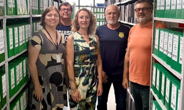 Três homens e duas mulheres posando para foto em meio a estantes com caixas de arquivos