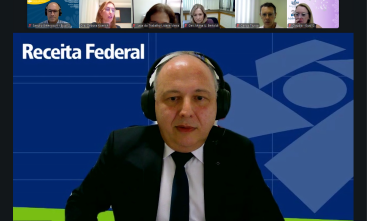 Print de tela de um homem grisalho de terno e gravata fazendo uma palestra por videoconferência