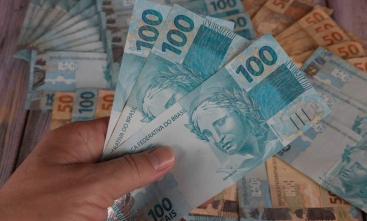 Foto de uma mão masculina segurando notas de cem reais.