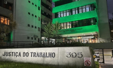Parte da fachada do TRT-SC iluminada de verde, mostrando três pavimentos. À frente, no chão, um letreiro escrito Justiça do Trabalho